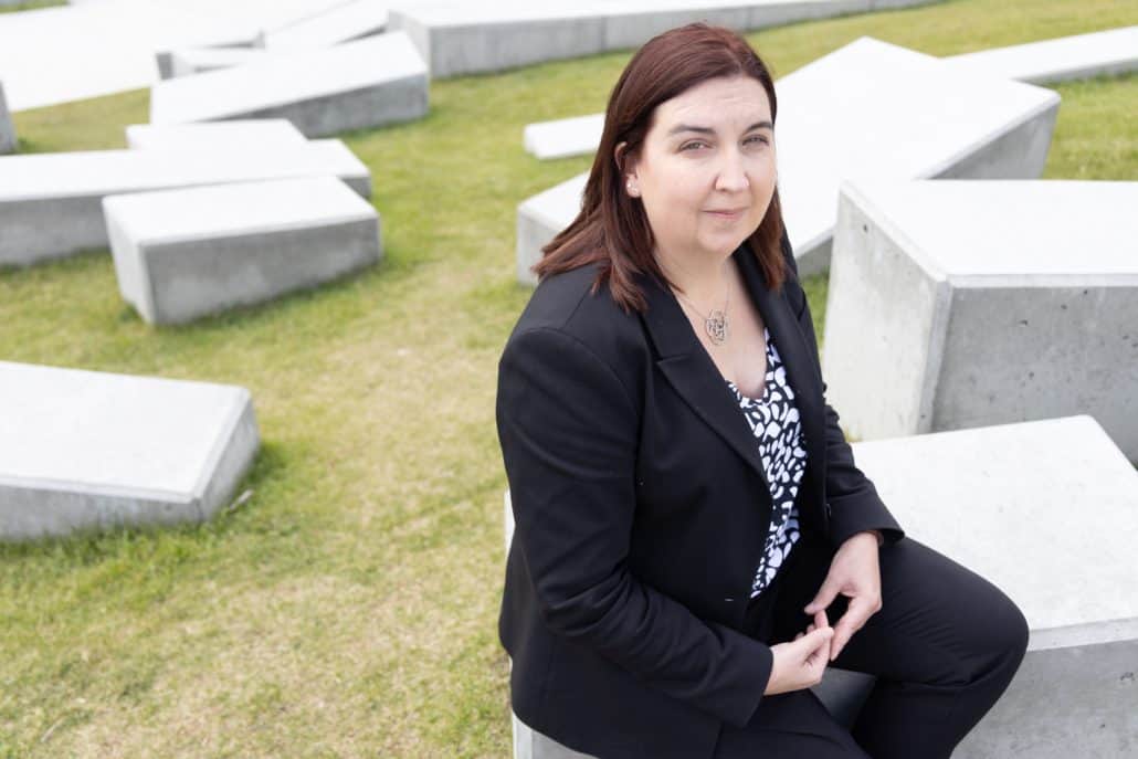 Women in black blazer sitting on concrete structure.