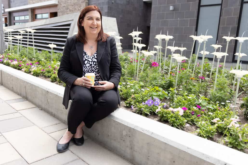 Woman sitting in front of flowers with a coffee in her hand.