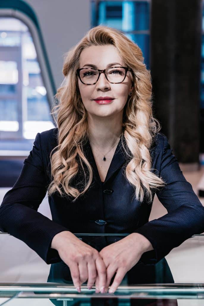 Woman with blonde hair and glasses looking into the camera.