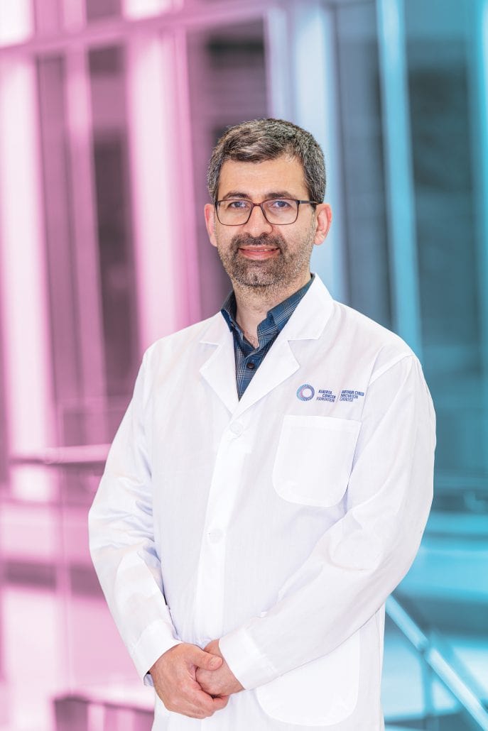 Male doctor in a white lab coat with a pink and blue background.
