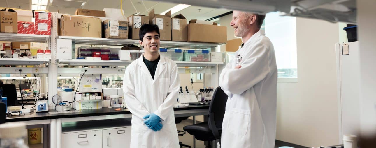 Two men in white coats looking at each other in a lab.