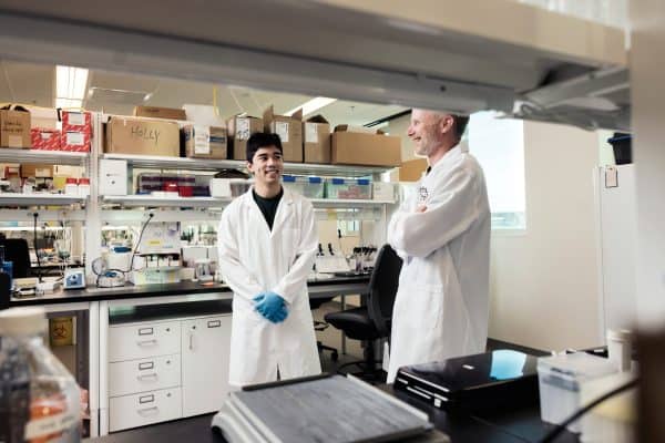 Two men in white coats looking at each other in a lab.