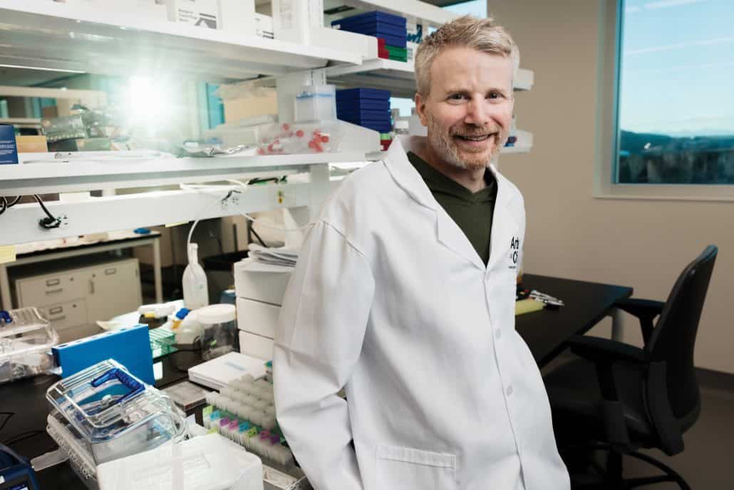 Man in white coat standing in a lab. 