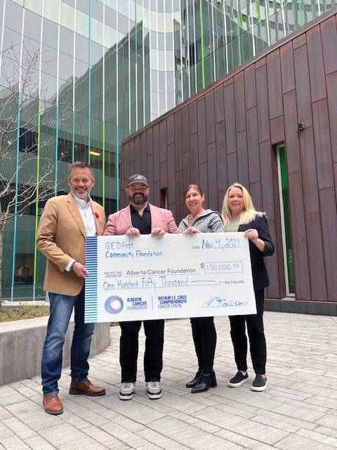 Four people stand holding a cheque. 