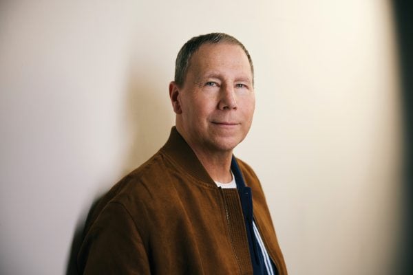 Man looks into the camera with beige wall behind him.
