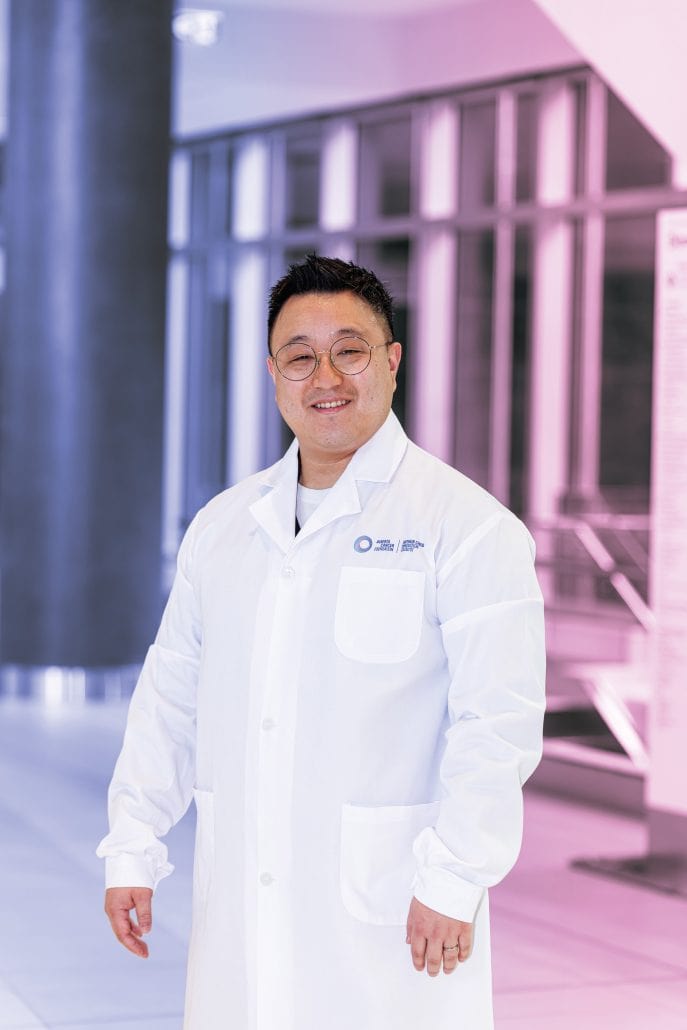 Male doctor in a white lab coat with a purple and pink background. 