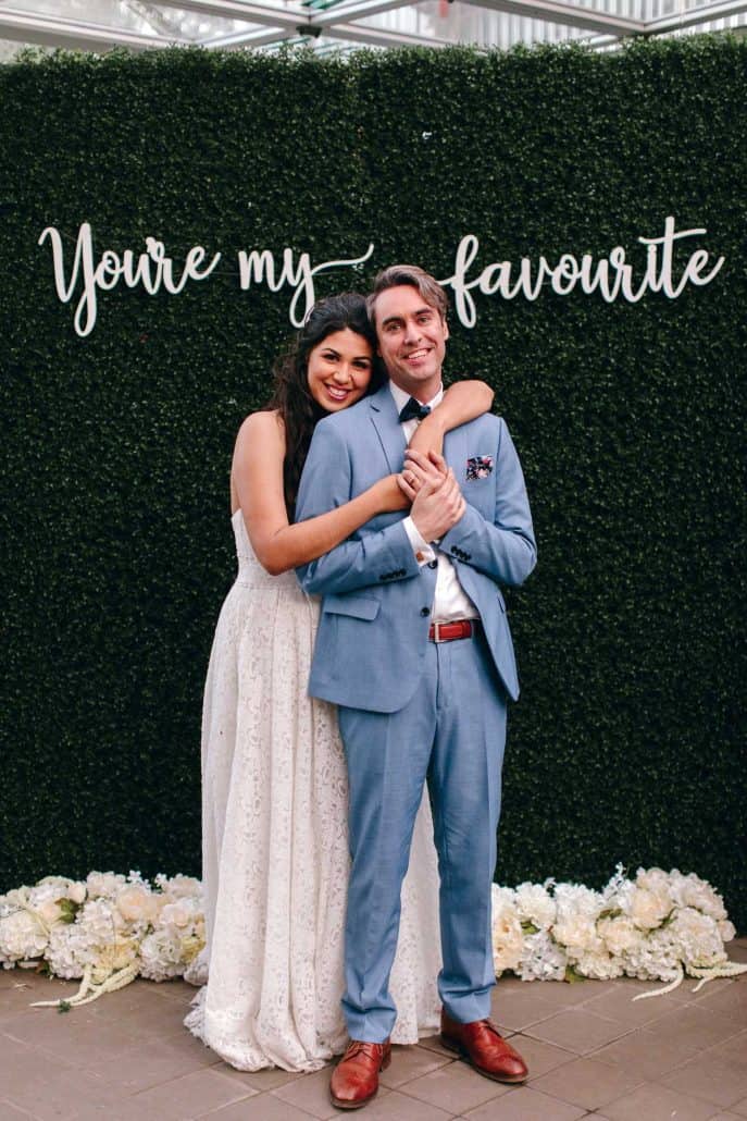 Woman in white dress hugging a man in a blue suit from behind.
