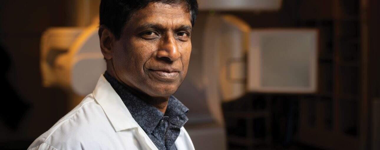 Doctor in white coat looking at the camera and standing in front of a radiation machine.