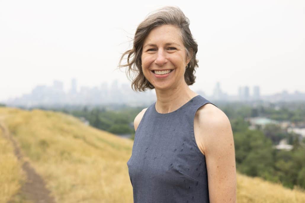 Woman standing outside with a city skyline behind her.