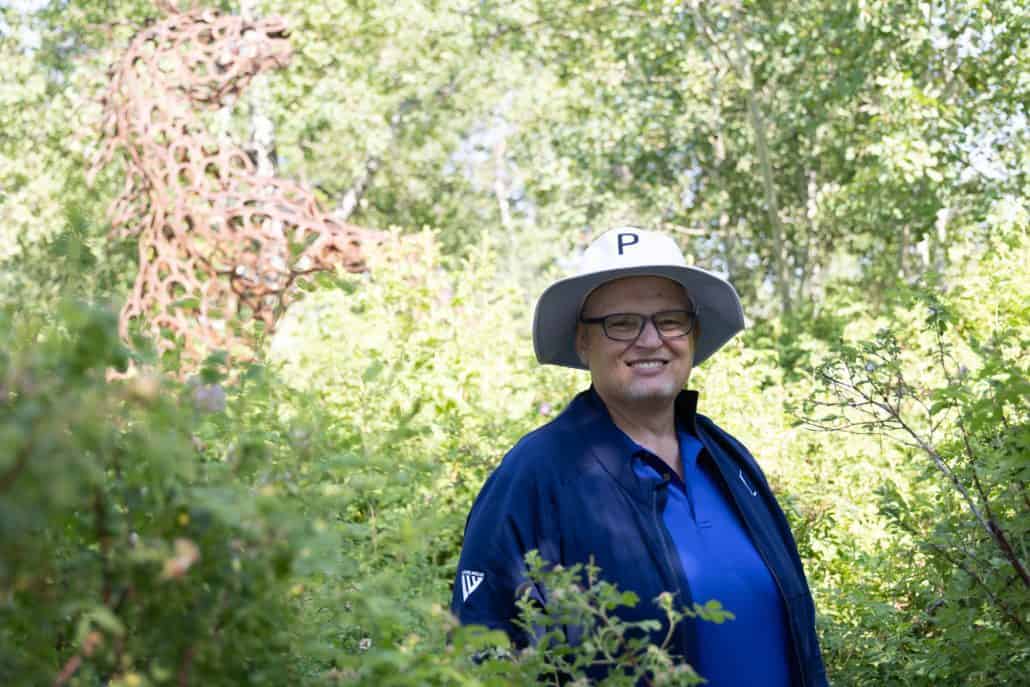 Man in blue shirt surrounded by green trees.
