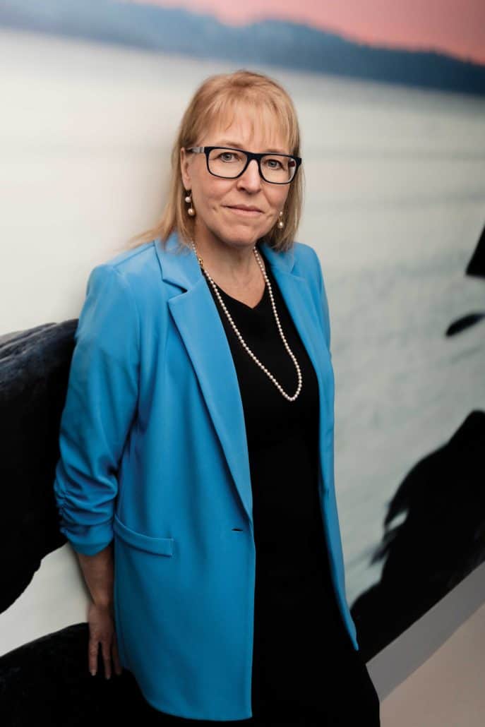 Woman in a blue blazer leaning against a wall.