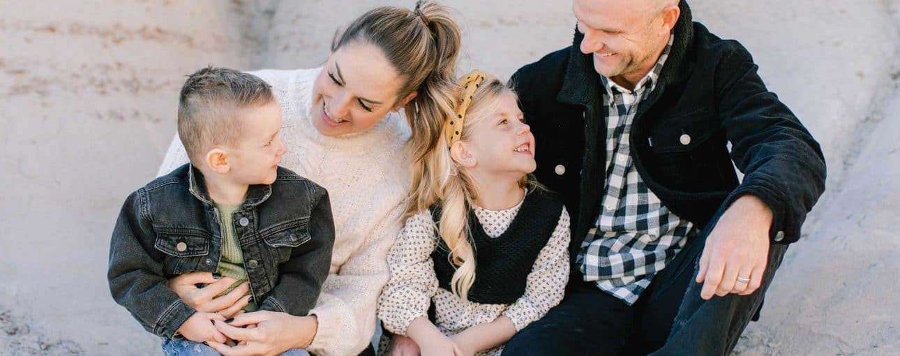 Young family with two kids sitting down looking at each other.