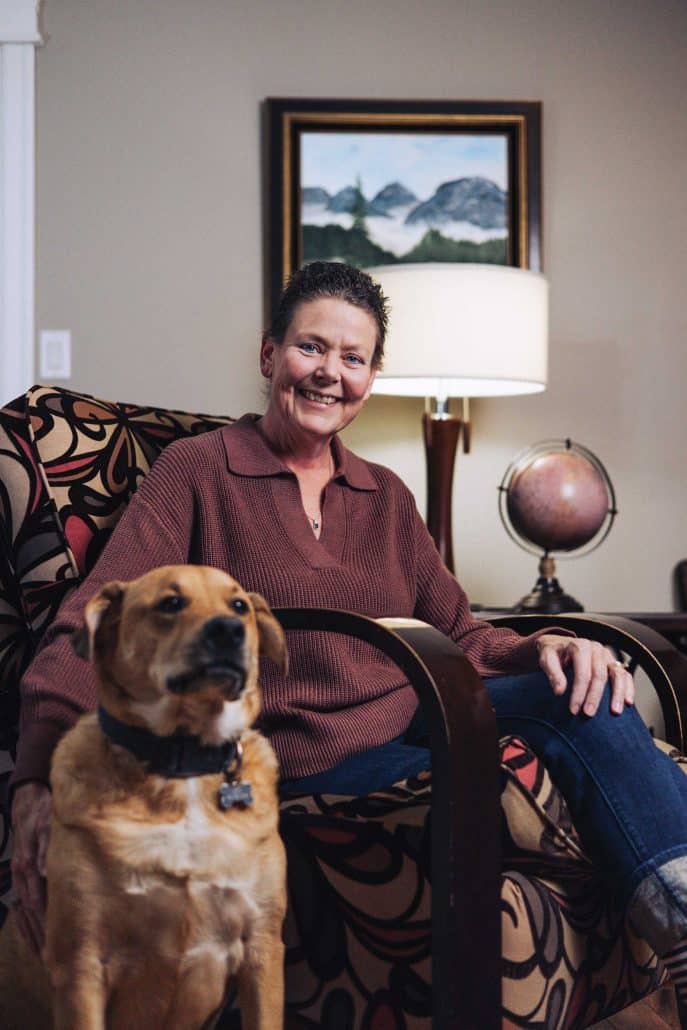 Woman sitting in a chair in her home with her dog.