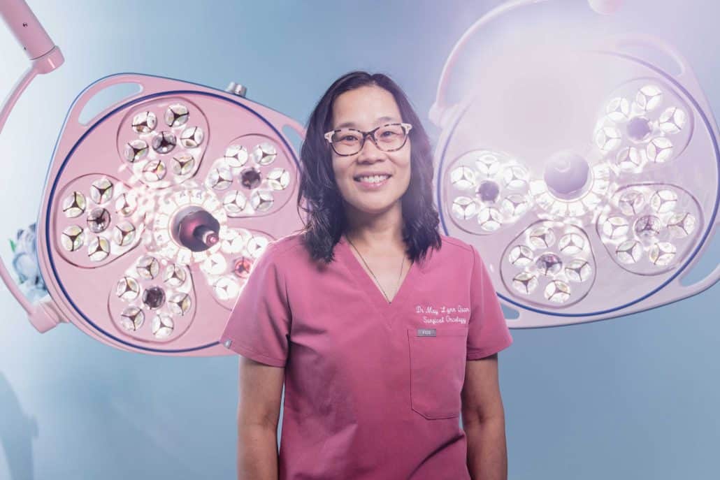 Doctor in pink scrubs standing in front of operating lights.