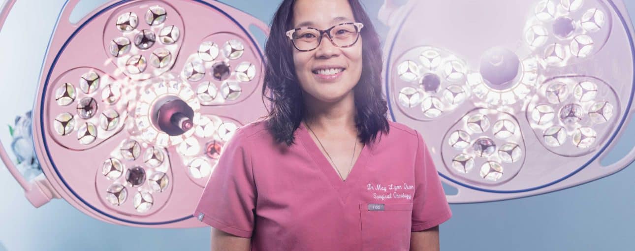Doctor in pink scrubs standing in front of operating lights.