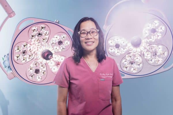 Doctor in pink scrubs standing in front of operating lights.