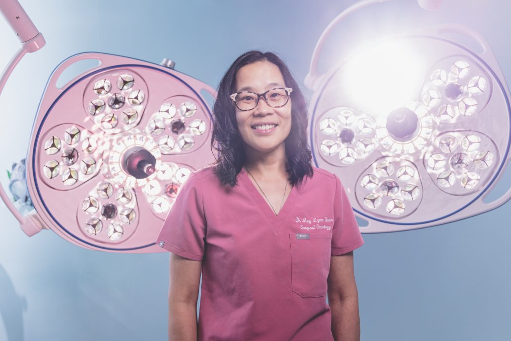 Doctor in pink scrubs in front of surgical lights.