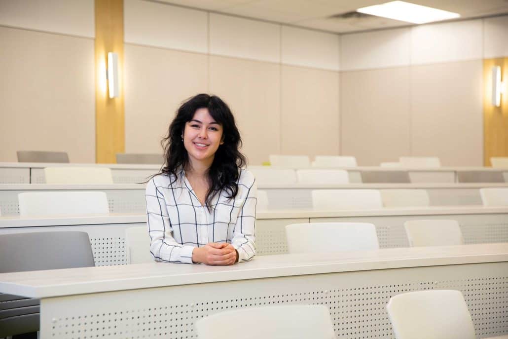 Woman sitting in a bright, empty classroom. 