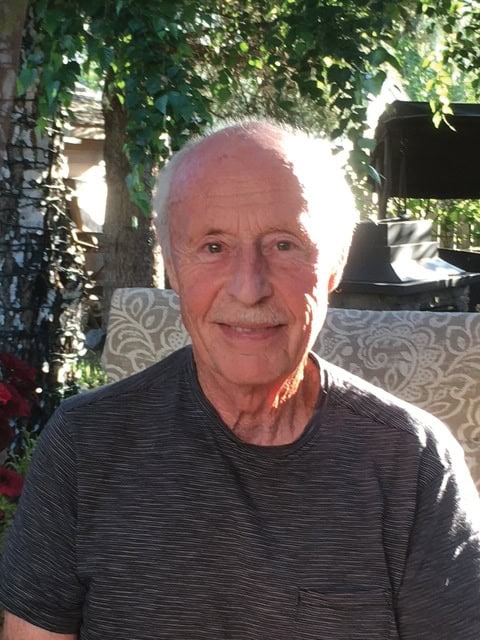 Elderly man smiling at the camera while sitting outside. 