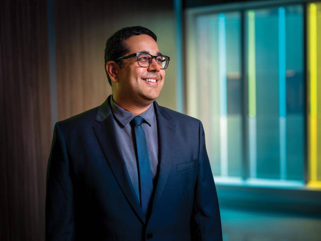 Man with glassed in a suit looking to his left. 
