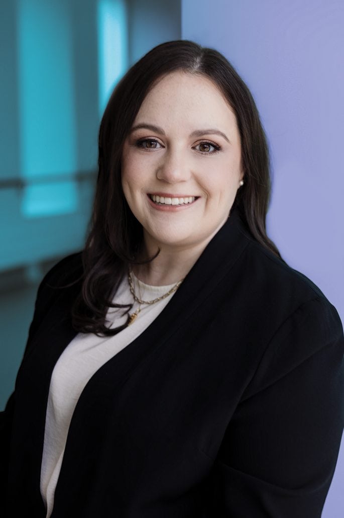 Female doctor in black blazer with a purple and blue background. 