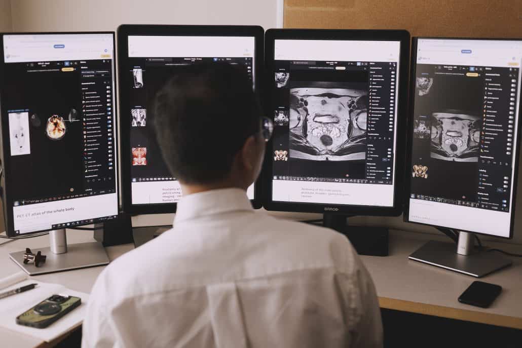 A doctor looking at four screens showing medical results. 
