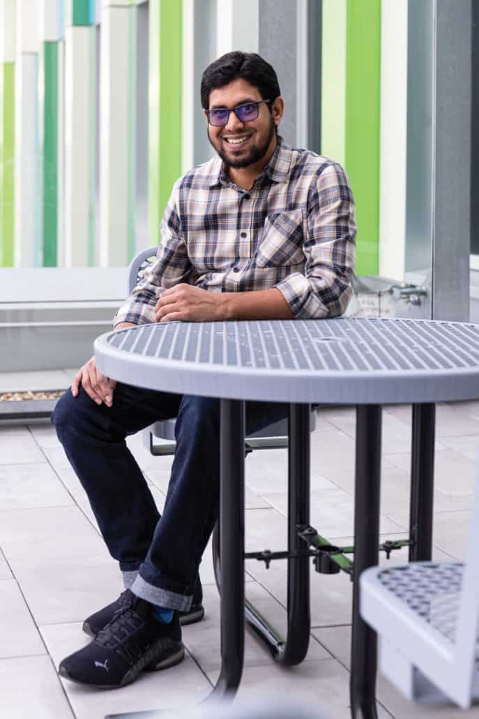 Man in checkered shirt sitting at an outside table.