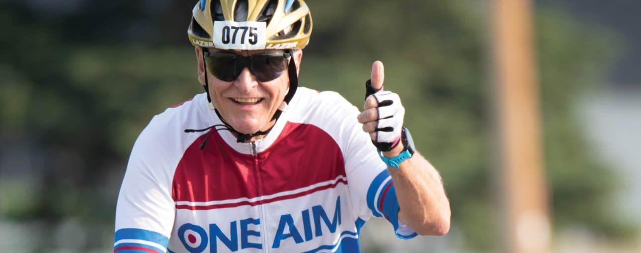 A man gives a thumbs up while riding his bike.