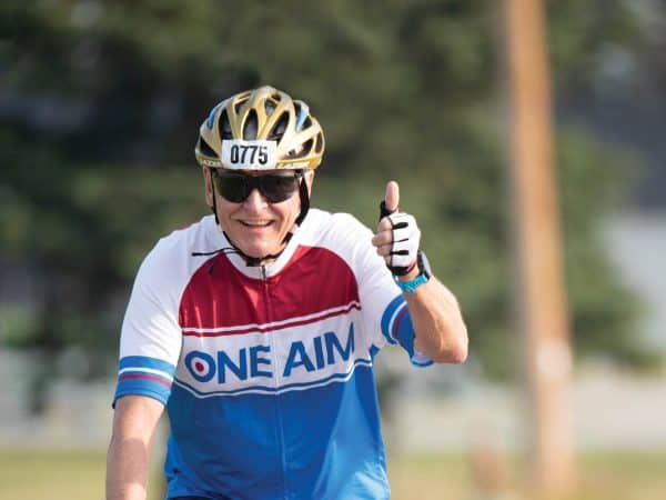 A man gives a thumbs up while riding his bike.