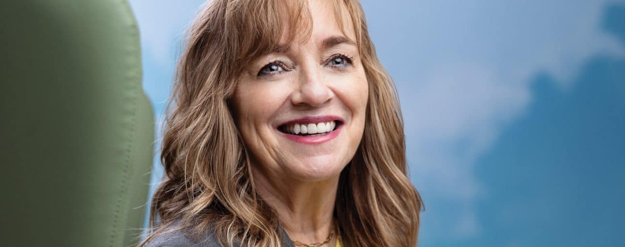 Woman sitting in a green chair smiling at the camera.