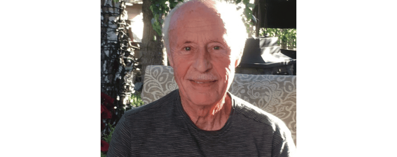 Elderly man smiling at the camera while sitting outside.